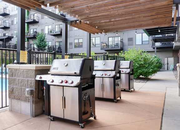 A patio with a grill and a pool in the background.