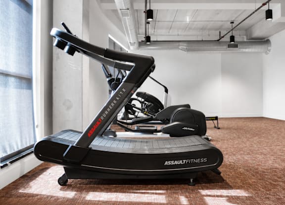 A black assault fitness treadmill in a room with white walls.