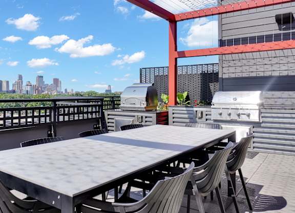 A table and chairs are set up on a balcony with a city skyline in the background.