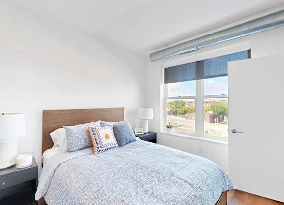 A bedroom with a bed, nightstand, and window.