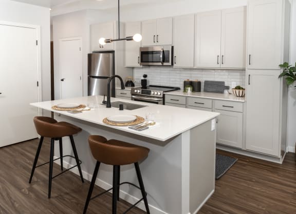 a kitchen with white cabinets and a white island with two stools