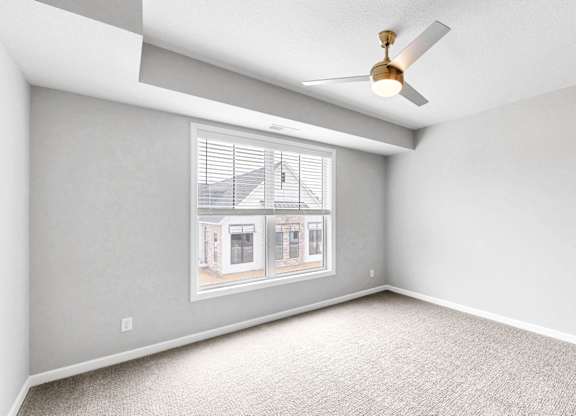 A room with a ceiling fan and a window showing a house.