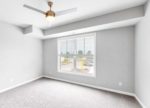 A room with a ceiling fan and a window showing a street view.