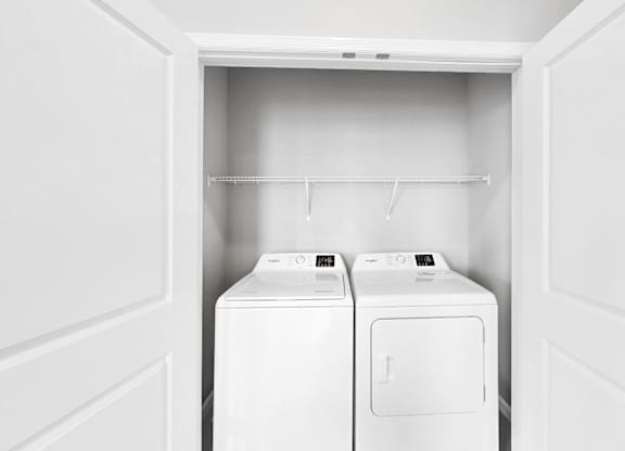 Two white washing machines in a white laundry room.