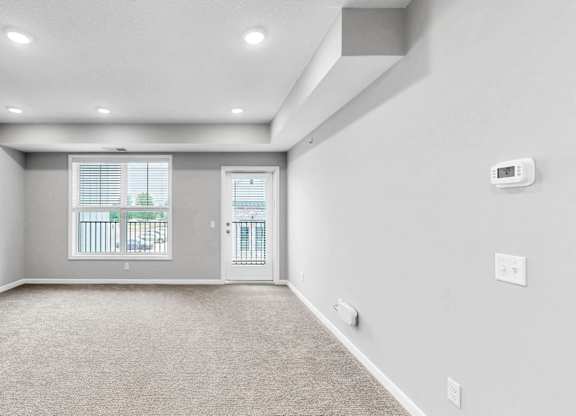 A spacious room with a carpeted floor and a window with blinds.