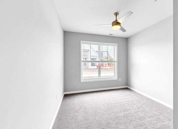 A room with a ceiling fan and a window overlooking a street.