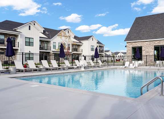 A swimming pool surrounded by lounge chairs and umbrellas in front of a building.