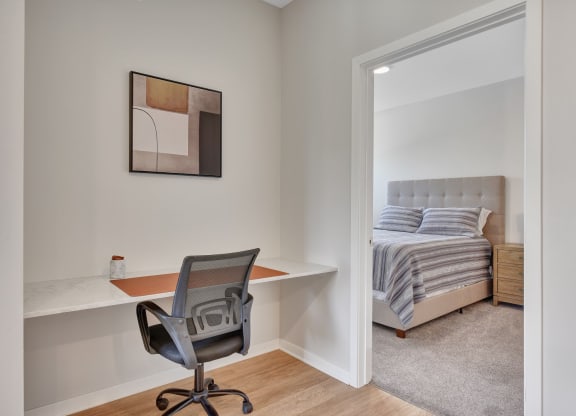 a home office with a desk and chair in a bedroom with a bed in the background