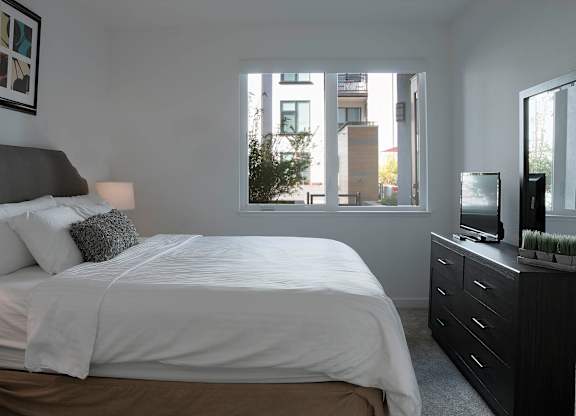 A bedroom with a large bed, a window with a view of a building, and a TV on a dresser at Catalyst Mountain View, Mountain View, CA