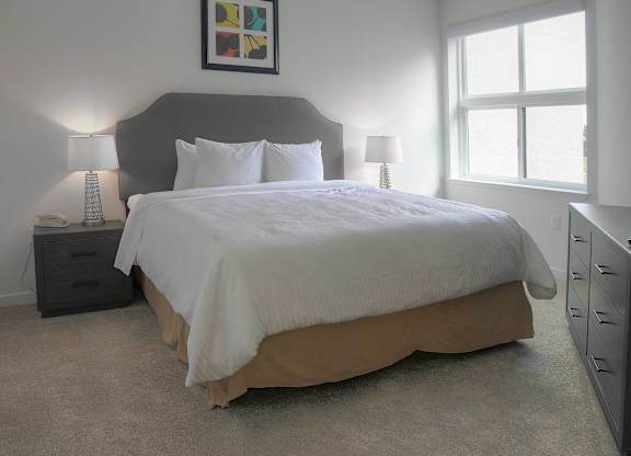 A bed with a white comforter and pillows is in a room with a grey headboard and a painting above it at Catalyst Mountain View, Mountain View, CA
