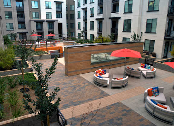 A patio with a red umbrella and white couches at Catalyst Mountain View, Mountain View, CA