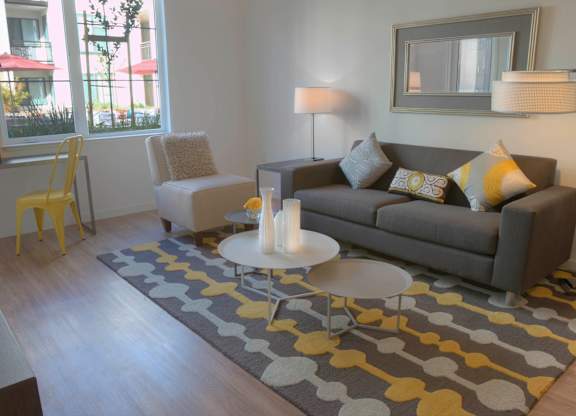 A grey couch with yellow and white pillows sits in a living room with a grey rug and a white coffee table at Catalyst Mountain View, Mountain View, CA
