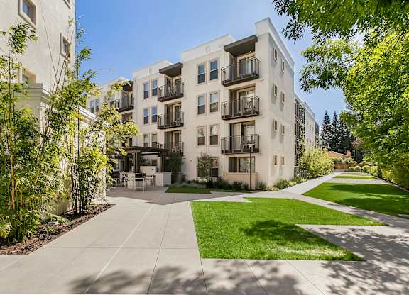 A sunny day at a modern apartment complex with a well-maintained lawn and trees. at Cirrus Redwood City Apartments, Redwood City