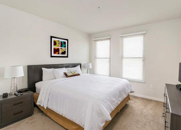 A bedroom with a large bed, a nightstand with a lamp, and a picture on the wall. at Cirrus Redwood City Apartments, Redwood City, CA, 94061