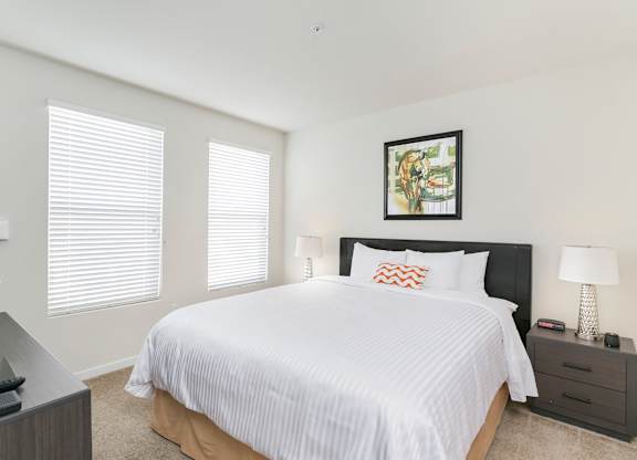 A bedroom with a large bed, a nightstand with a lamp, and a picture on the wall. at Cirrus Redwood City Apartments, Redwood City, CA, 94061