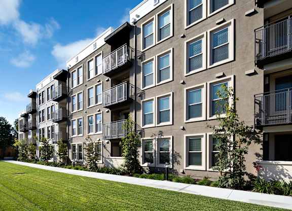 Apartment building with balconies and green lawn in front. at Cirrus Redwood City Apartments, California