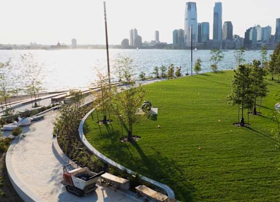 A park with a grassy area and a city skyline in the background at One West,  New York,10004