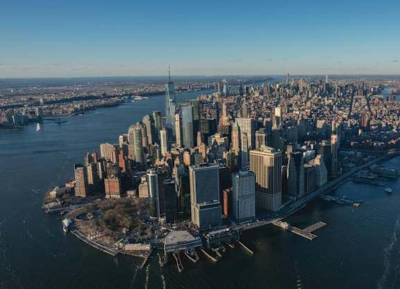 A cityscape with a body of water in the foreground and a clear blue sky above. at One West,New York, NY