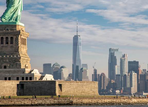The Statue of Liberty stands tall in front of the skyline of New York City. at One West, New York, NY,10004