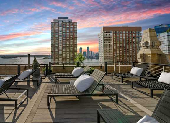 A rooftop patio with lounge chairs and a view of the city skyline at sunset at One West,  New York,10004.