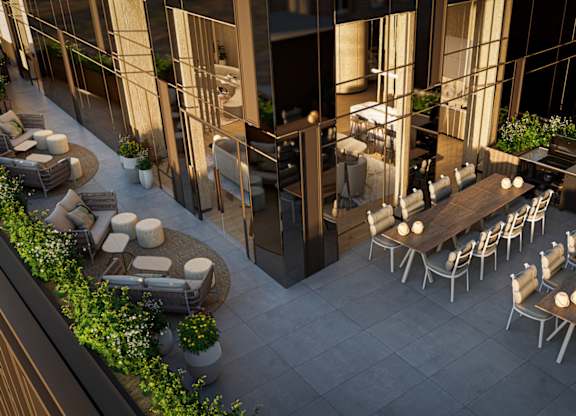 A patio with tables and chairs is surrounded by plants and buildings.