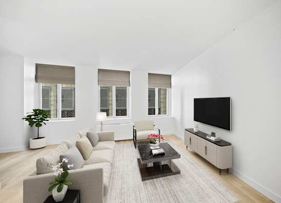 A living room with a grey couch, a coffee table, and a flat screen TV mounted on the wall at Aria, New York, 10038