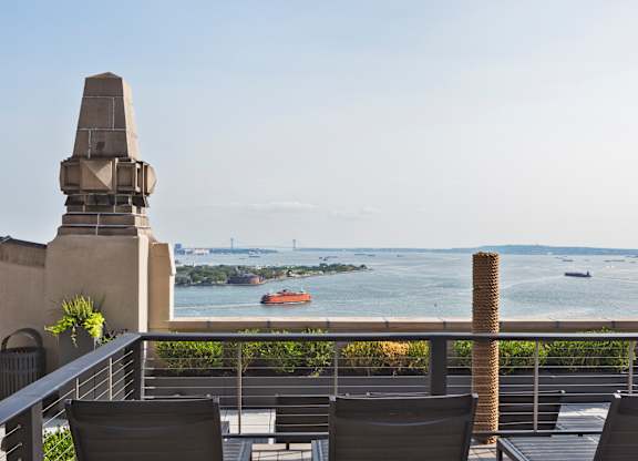 A balcony with chairs and a view of a bay with boats at One West,  New York,10004.