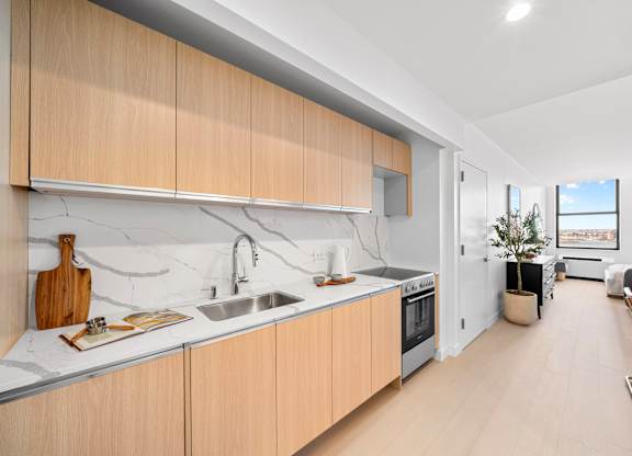 A modern kitchen with wooden cabinets and a marble countertop at One West, New York, NY,10004.
