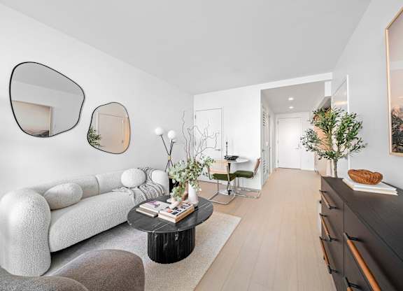 A modern living room with a white sofa, a black coffee table, and a large mirror on the wall at One West,New York, NY.