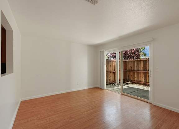 A room with wooden floors and a sliding glass door leading to a backyard.