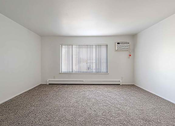 A room with a carpeted floor and a window with blinds.