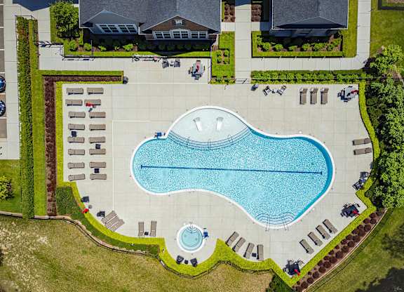 An aerial view of a swimming pool surrounded by lounge chairs and greenery.