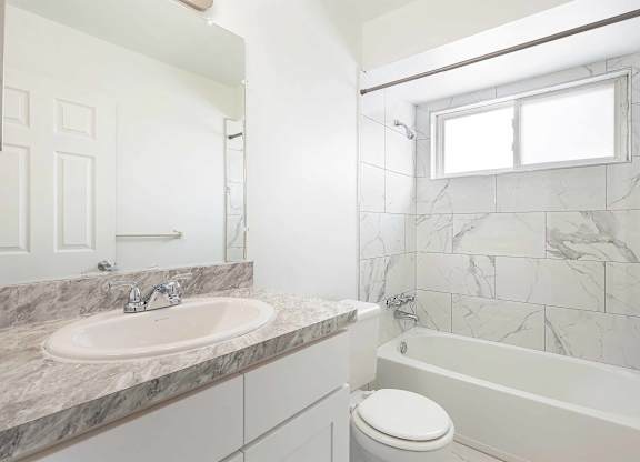 A white bathroom with a marble countertop and a white toilet.