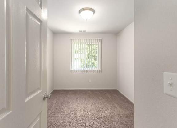 A room with a carpeted floor and a window with blinds.