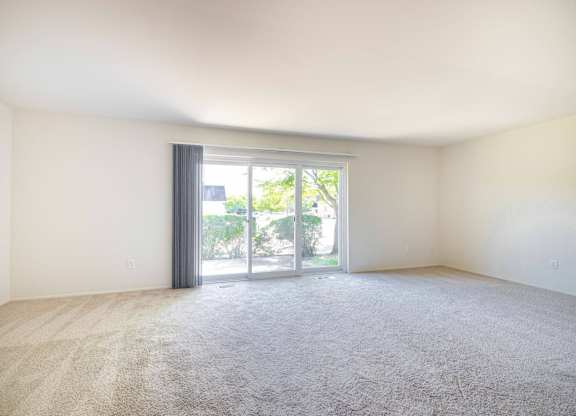 A room with a carpeted floor and a sliding glass door leading to a patio.