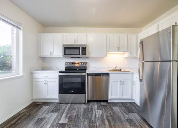 A kitchen with white cabinets and a wood floor.