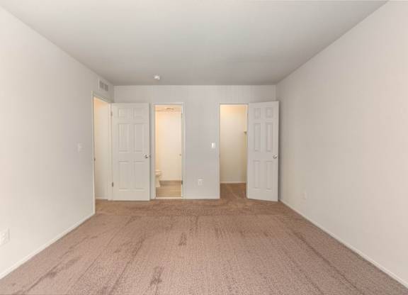 A room with white walls and carpeted floor with three white doors.