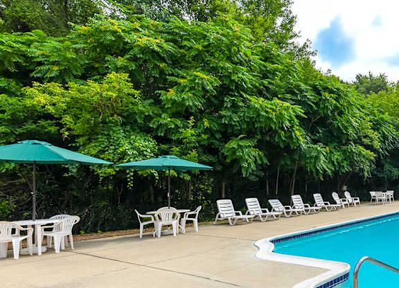 A pool surrounded by trees and chairs.