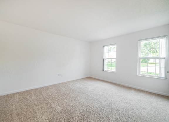 A room with a carpeted floor and two windows.