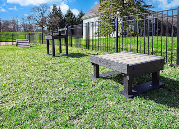 A wooden bench sits in a grassy field next to a metal fence.