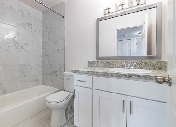 A white bathroom with a marble counter top and a large mirror.