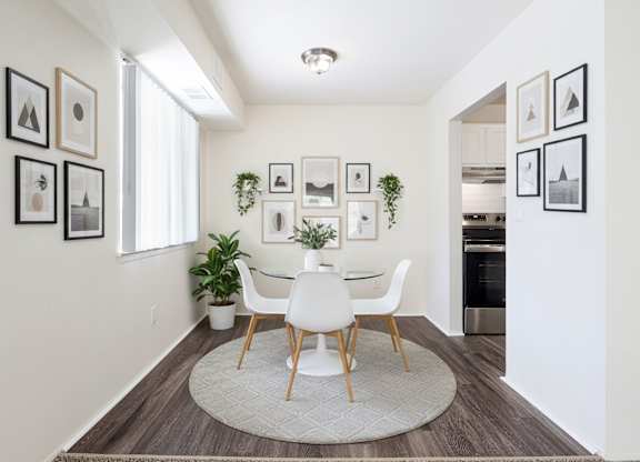 A white dining table with four chairs is in the middle of a room with a rug on the floor.