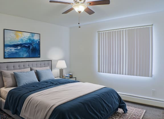 A bedroom with a bed, a ceiling fan, and a painting on the wall.