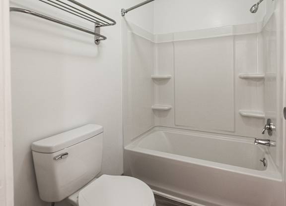 A white toilet sits next to a white bathtub in a small bathroom.