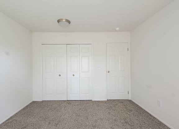 A room with two white doors and carpeted floor.