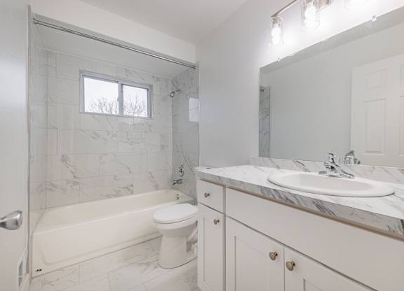 A white bathroom with a marble counter top and a tub.