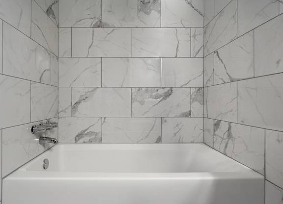 A white bathtub with a marble tile wall.
