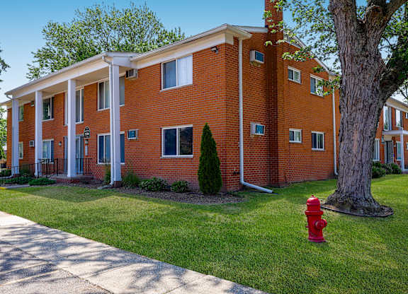 A red fire hydrant sits on a green lawn in front of a red brick building.