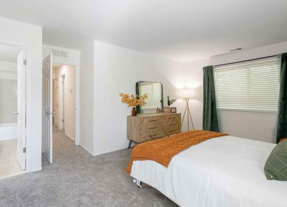 A bedroom with a bed, nightstand, and a window with green curtains.