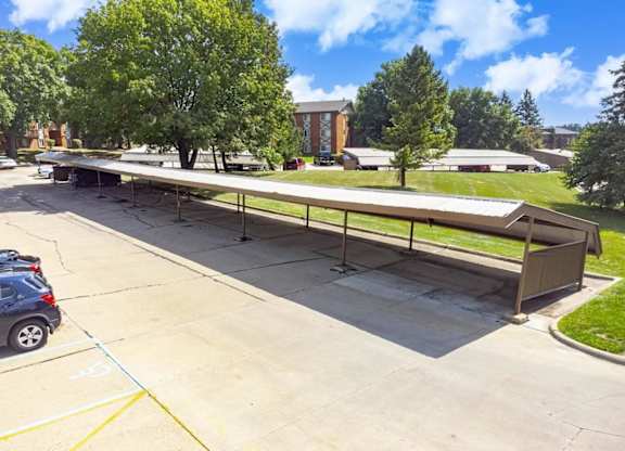 A long outdoor picnic table is surrounded by a parking lot.